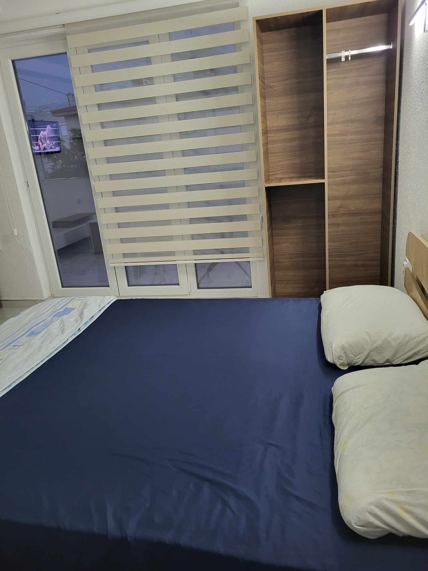 Une chambre à coucher avec un lit, une armoire en bois et une fenêtre avec des stores.