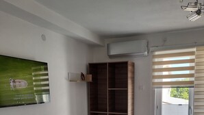 Una habitación moderna con pared blanca, un mueble de madera, televisión integrada y puerta corredera de vidrio.