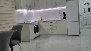 Een moderne keuken met lichte kastjes, een witte koelkast en een marmeren aanrecht. Er staat een grijze bekleden stoel en een klein eiland met een spoelbak.