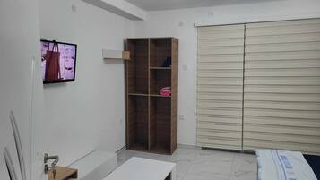 Camera da letto moderna con un letto bianco, un armadio in legno, una TV montata a parete e un guardaroba con ante scorrevoli.