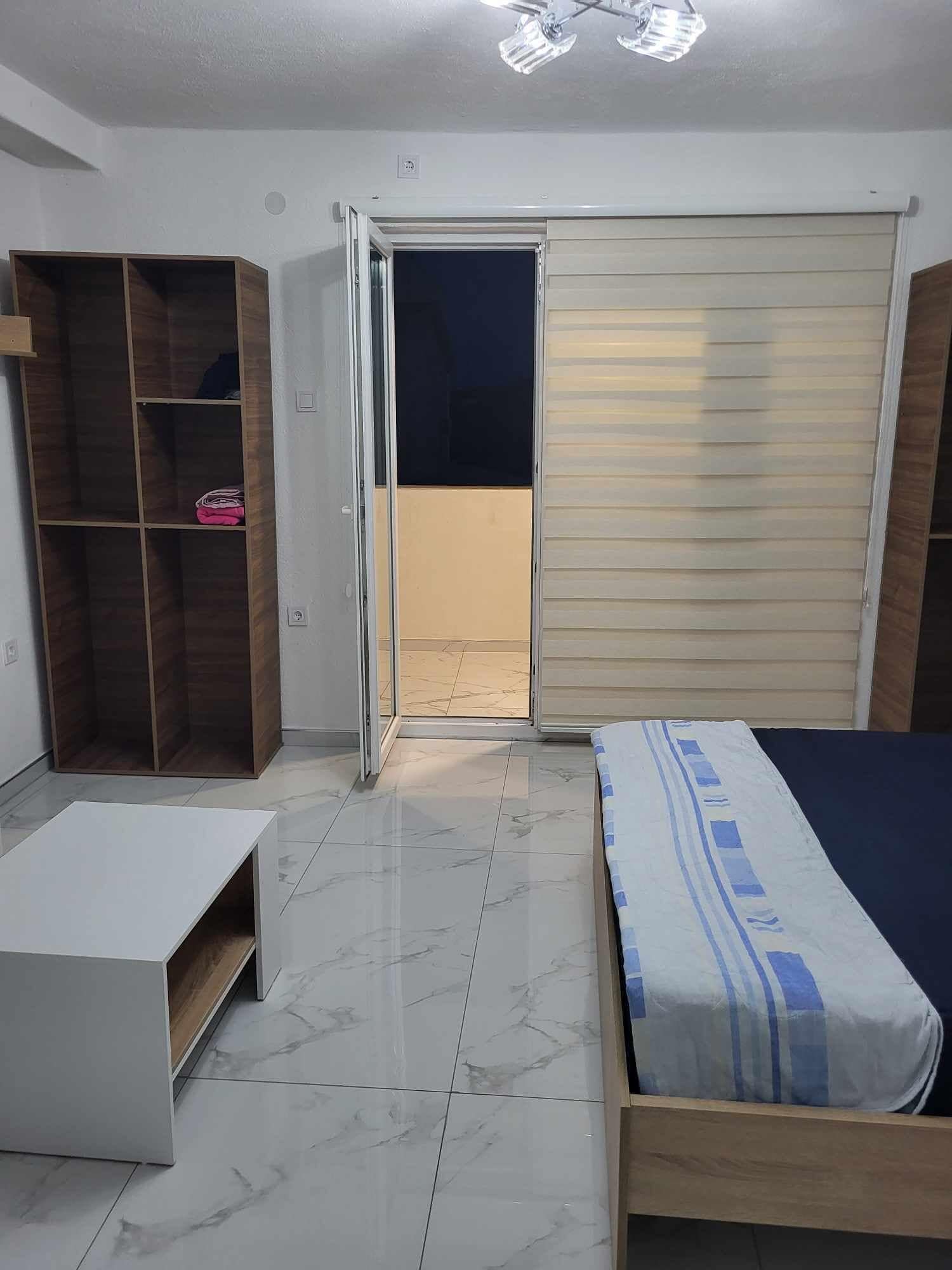 Un dormitorio con cama, armario, escritorio y puerta corredera a un balcón.