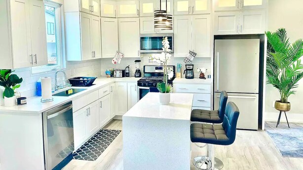 A modern kitchen with white cabinets, a central island, a built-in oven, and a refrigerator. - Luxurious Getaway Home with Rooftop Patio 10mins to downtown Durham and Duke (Durham)