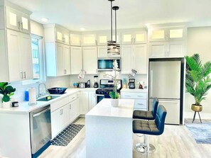 A modern kitchen with white cabinets, a central island, a built-in oven, and a refrigerator.