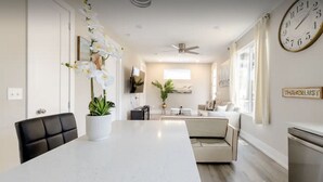 A modern kitchen with a central island, a dining area with a black chair, and a living space with a sofa and a TV. - Luxurious Getaway Home with Rooftop Patio 10mins to downtown Durham and Duke (Durham)
