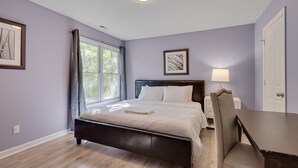 Ein Schlafzimmer mit Bett, Nachttisch, Stuhl, Fenster mit Vorhängen und einer Tür.