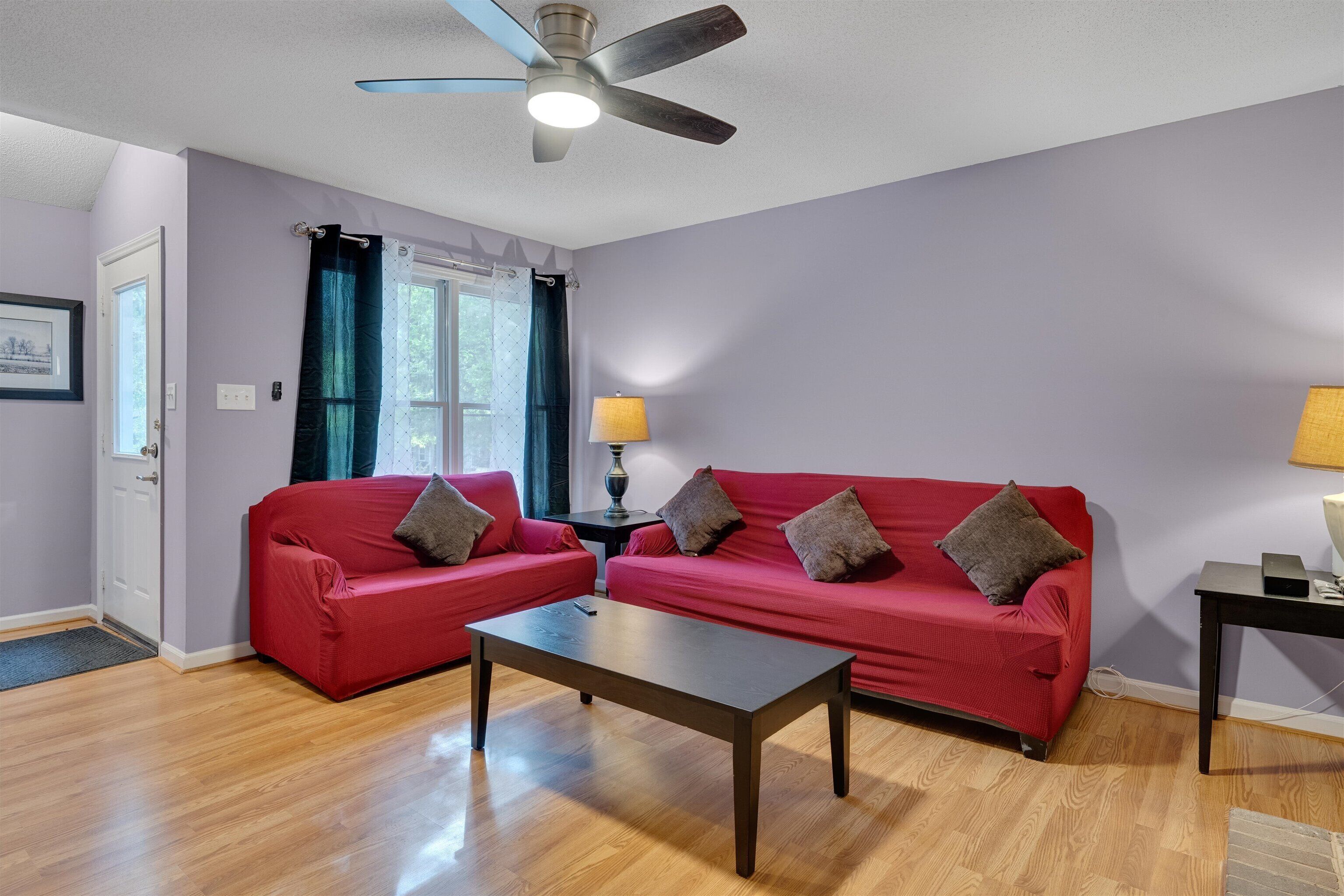 A living room with two red sofas, a wooden coffee table, a ceiling fan, and a lamp on a side table.