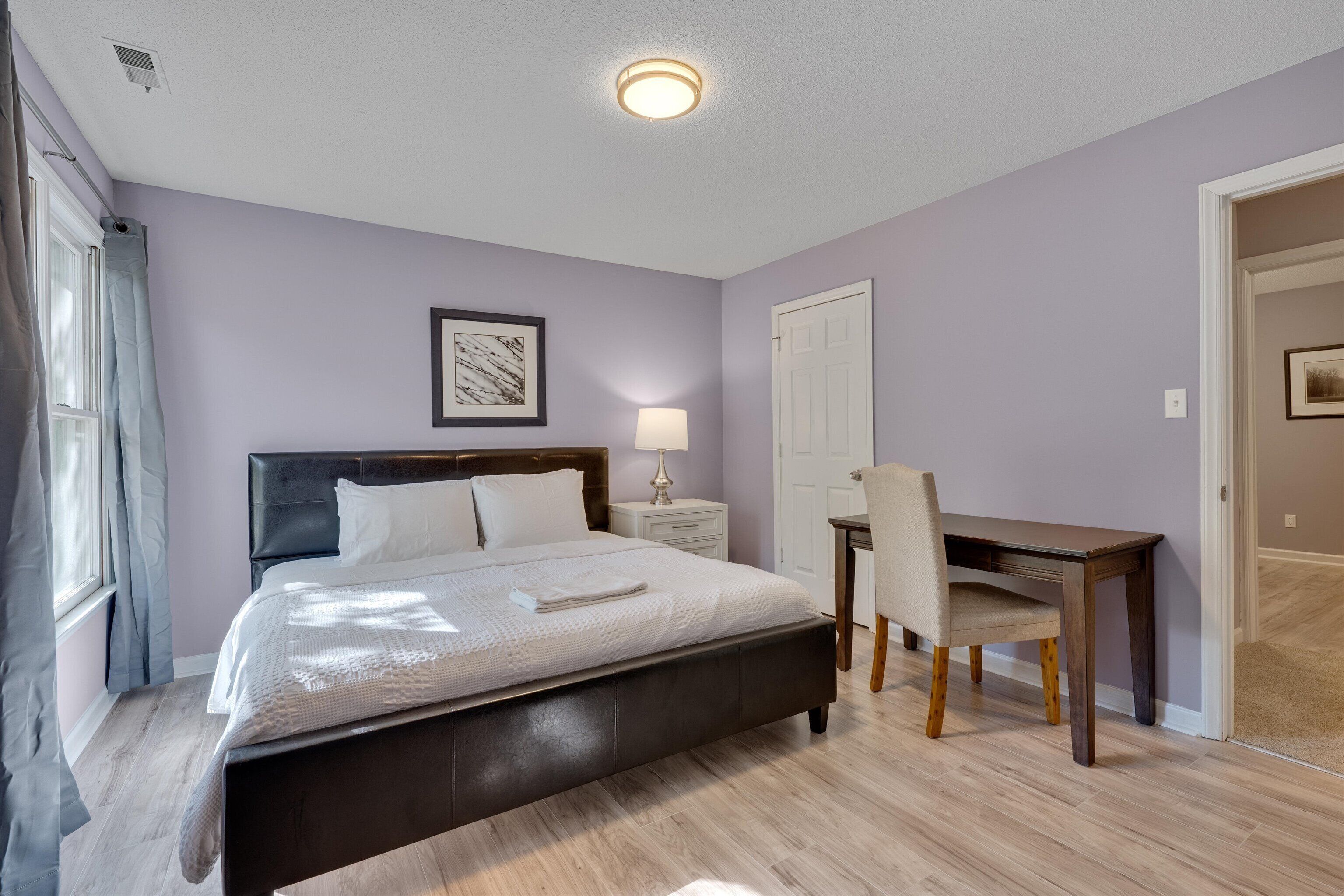 Een slaapkamer met een bed, nachtkastje, lamp, stoel en een deur.