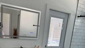 Ein modernes Badezimmer mit einem weißen Waschtisch, einem großen Spiegel, einer Toilette und einem Fenster.