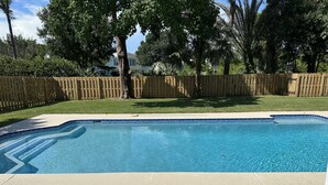 Ein rechteckiger Pool mit Fliesenrand, umgeben von einem Holzzaun und einer Rasenfläche.
