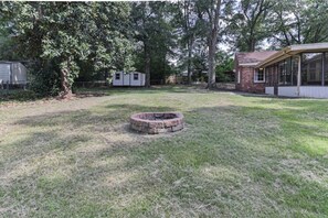 Relax by the fire pit in a serene backyard with a grassy lawn and shaded trees.