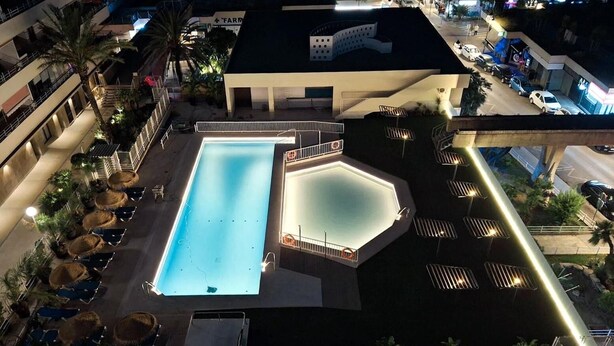 Vue aérienne d’un hôtel doté d’une grande piscine rectangulaire, d’une plus petite piscine octogonale et d’une terrasse sur le toit aménagée avec des chaises longues et des parasols.