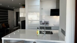 Une cuisine moderne dotée d’un îlot central, d’appareils électroménagers intégrés et d’un téléviseur à écran plat.