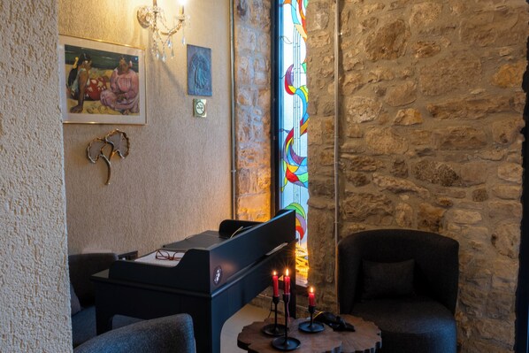 A cozy room with a piano, a stone wall, a stained glass window, and a small table with candles. - Void Urla (Urla)