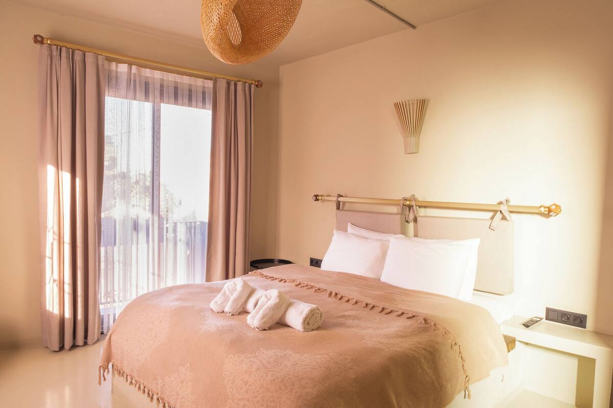 A hotel room with a bed, curtains, a bedside table, and a wall-mounted light fixture.