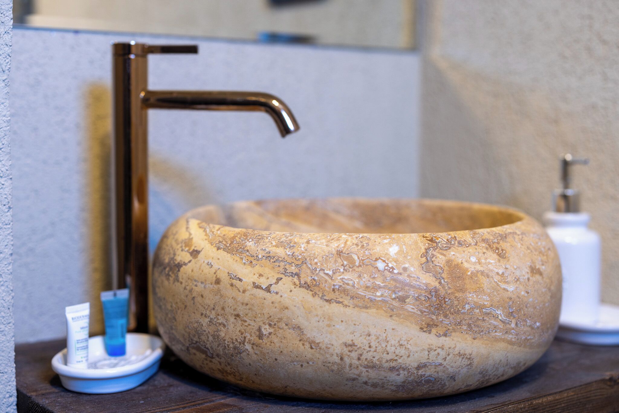A bathroom with a round stone sink, a faucet, and a soap dispenser on a wooden countertop.