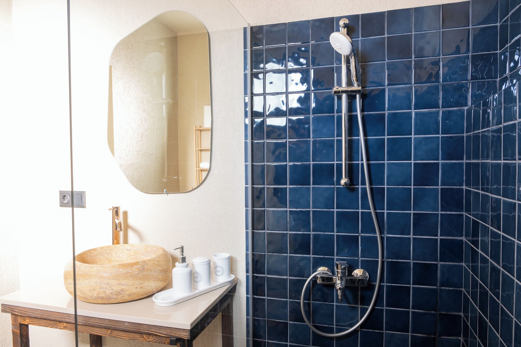 A bathroom with a round sink, a mirror, and a shower with blue tiles.
