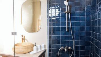 Un baño con un lavabo redondo, un espejo y una ducha con azulejos azules.