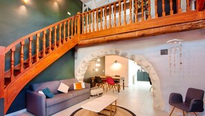 A spacious living area with a wooden staircase, a sofa, a coffee table, and a dining area with chairs. - Belle Maison Charmante Typiquement Provençale (Meyrargues)