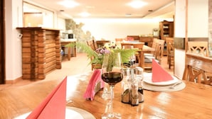 A dining area with a wooden table set for two, a glass of red wine, salt and pepper shakers, and a small potted plant with purple flowers. - Pensiunea Cornelia (Predeal)