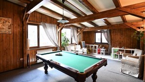 A pool table in a room with wooden walls and a sloped ceiling. There are chairs and a small table in the background. - Pensiunea Cornelia (Predeal)