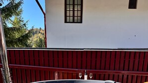 A wooden hot tub with a bench in front, surrounded by a wooden fence and a white building in the background. - Pensiunea Cornelia (Predeal)