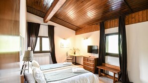 A bedroom with a wooden ceiling, a bed with white bedding, a desk with a chair, a TV, and a window with curtains. - Pensiunea Cornelia (Predeal)
