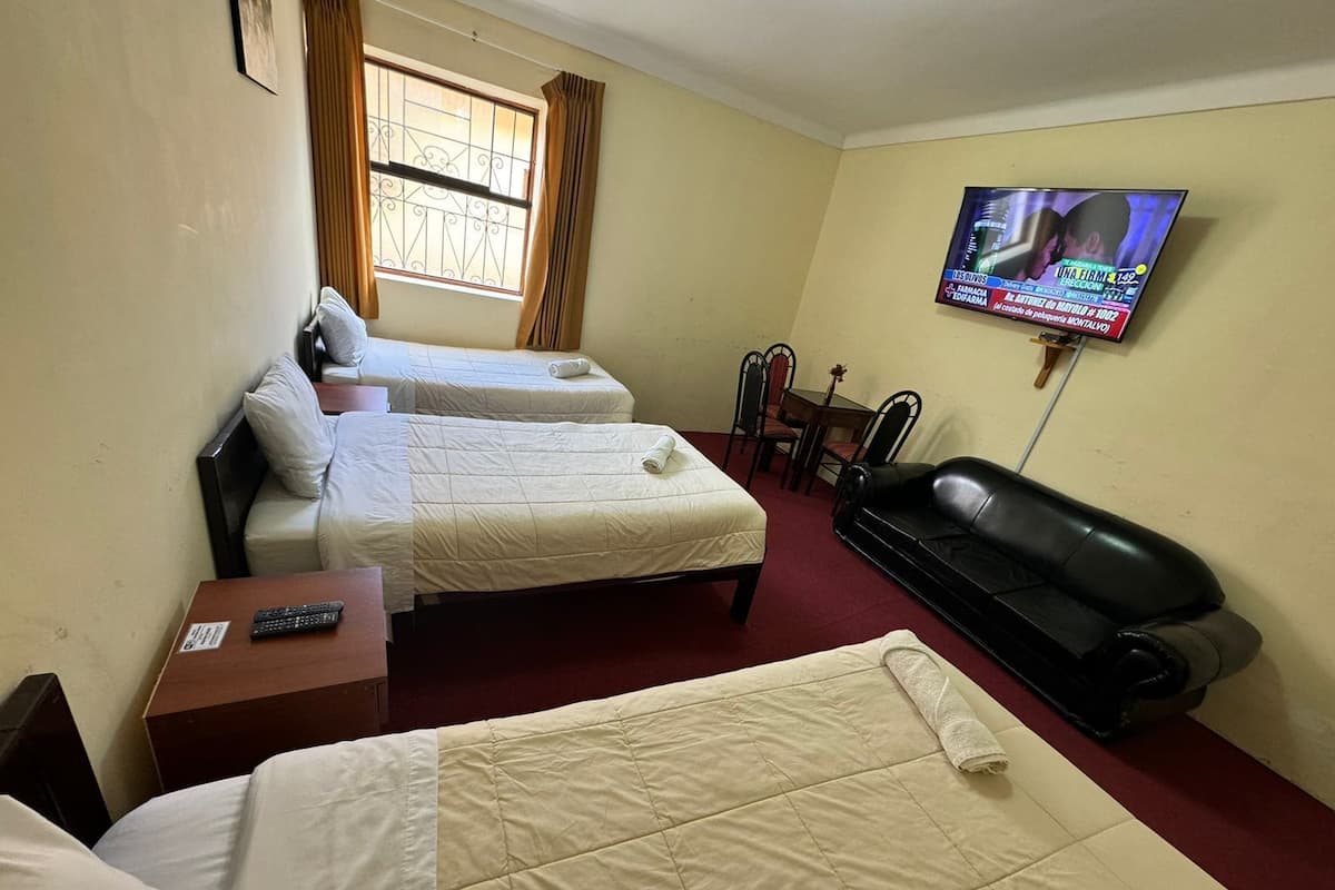 A hotel room with two beds, a TV, a black leather sofa, and a window with curtains.