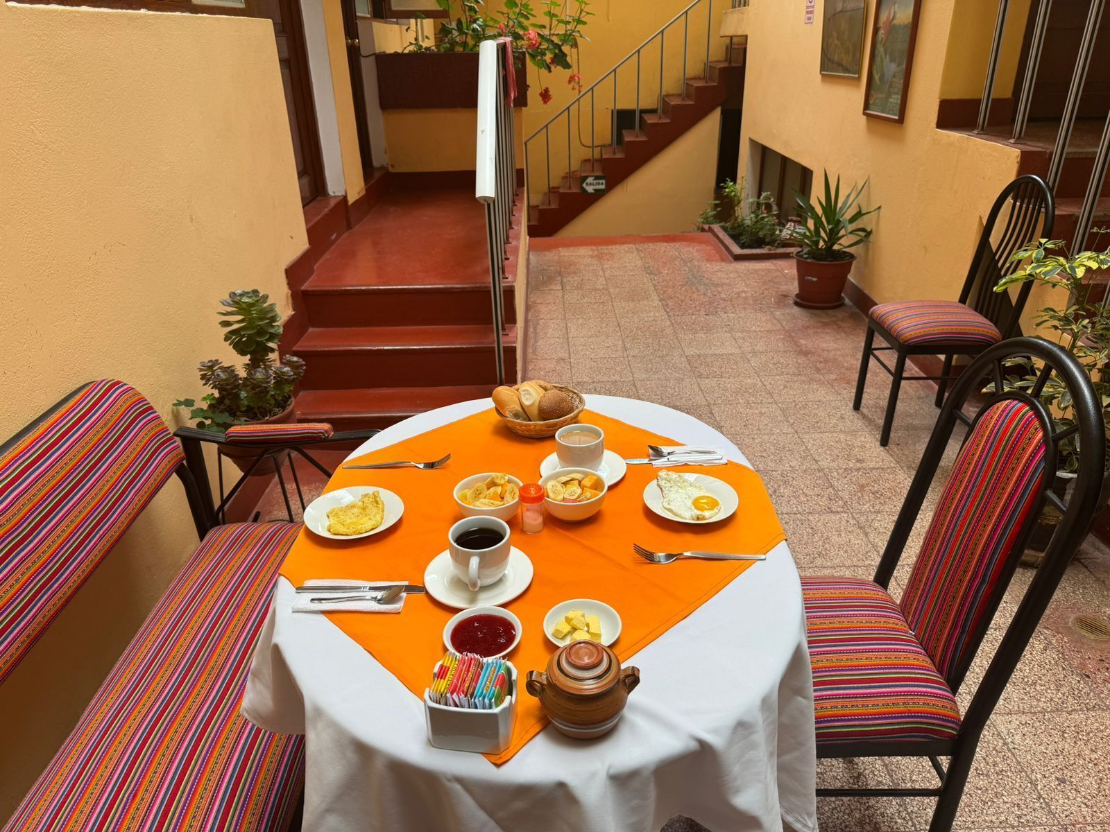 A round table with a white tablecloth and orange placemat, surrounded by colorful striped chairs.