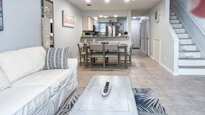A modern living room with a sofa, a coffee table, and a dining area with chairs and a table. - Destin/Miramar Beach Townhouse, 3-Min Walk to Sand, Sleeps 6, Pet Friendly (Miramar Beach)