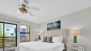 A bedroom with a large bed, two bedside tables, a ceiling fan, and a window with a view of buildings. - Destin/Miramar Beach Townhouse, 3-Min Walk to Sand, Sleeps 6, Pet Friendly (Miramar Beach)