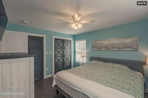 Un dormitorio con cama, ventilador de techo, ventana con persianas y una puerta.