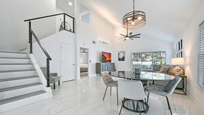 A spacious living area with a dining table, chairs, a staircase, and a ceiling fan. - Spacious+cozy house, near the beach, heated pool. (Naples)