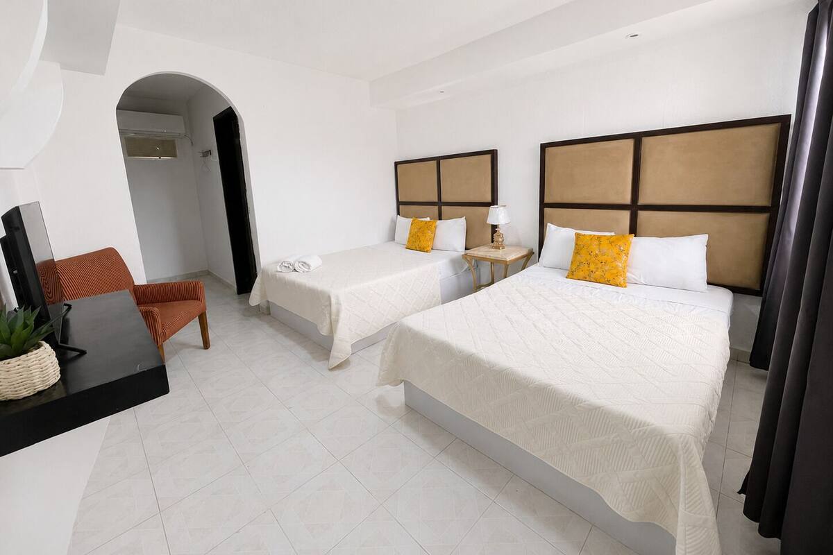 A hotel room with two beds, a desk, a chair, and a TV.