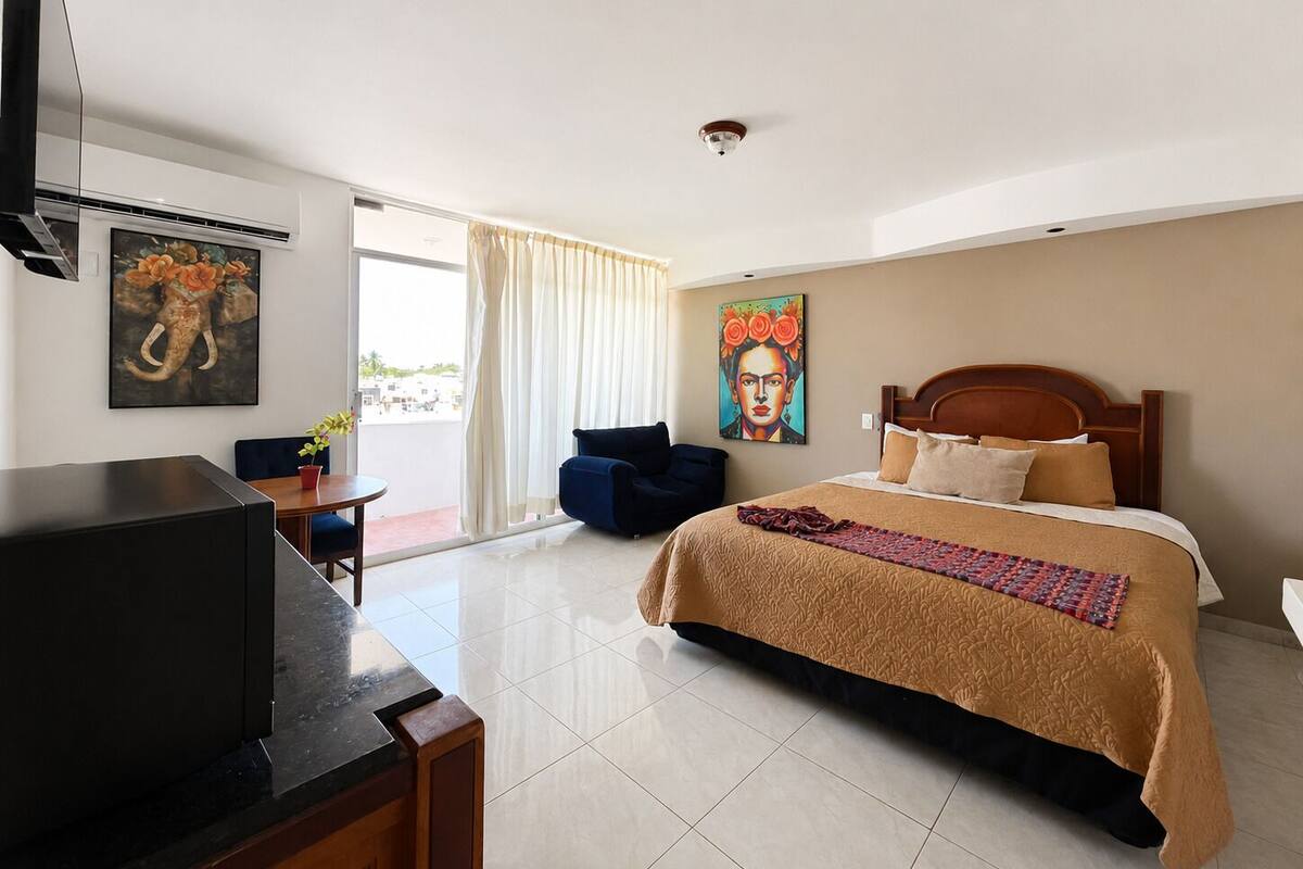A hotel room with a bed, a desk, a chair, a TV, and artwork on the walls.