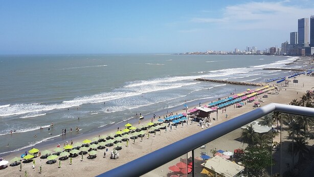 Una playa con sombrillas y gente, un horizonte urbano de fondo y un cielo despejado.