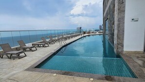 Una piscina en la azotea con sillones de descanso y vista al océano.