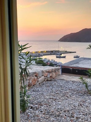 Vue d’une marina au coucher du soleil, avec des bateaux amarrés, un mur de pierre et un premier plan rocheux.