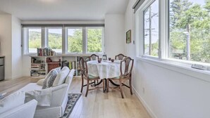 Amplia habitación con un gran comedor, un sofá y una estantería. Cuenta con ventanas amplias que ofrecen luz natural y vistas a árboles.