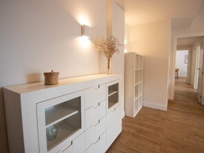 Una habitación moderna y minimalista con una consola blanca, un florero con flores secas y un estante blanco alto.