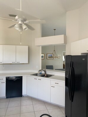 A modern kitchen with white cabinets, a black refrigerator, a dishwasher, and a ceiling fan. - Beautiful lake views in this 3BR/2Bath Condo in gated community in North Naples. (Naples)