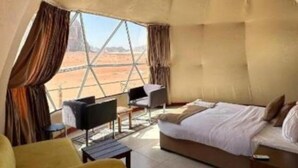 A spacious tent-like room with a bed, seating area, and a view of the desert landscape.