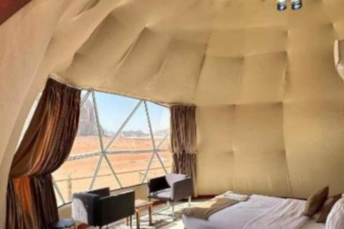 Een ruime, tentachtige kamer met een bed, zithoek en uitzicht op het woestijnlandschap.