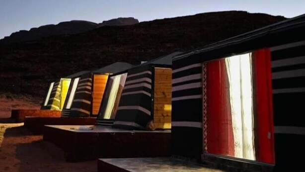 A row of modern, rectangular buildings with large windows, set against a desert landscape at dusk.