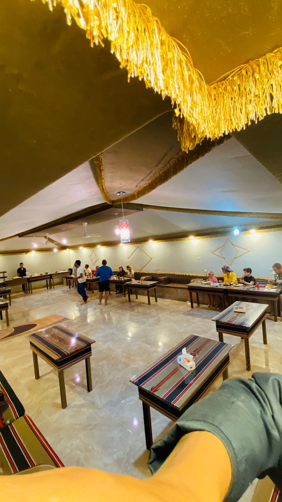 Un comedor interior con mesas y sillas, un techo alto con luces colgantes y una estructura de techo visible.