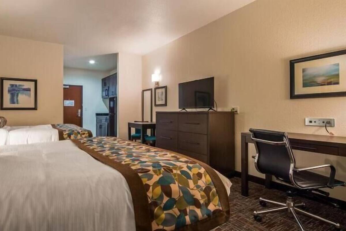 A hotel room with two beds, a desk with a chair, a television, and a dining area.