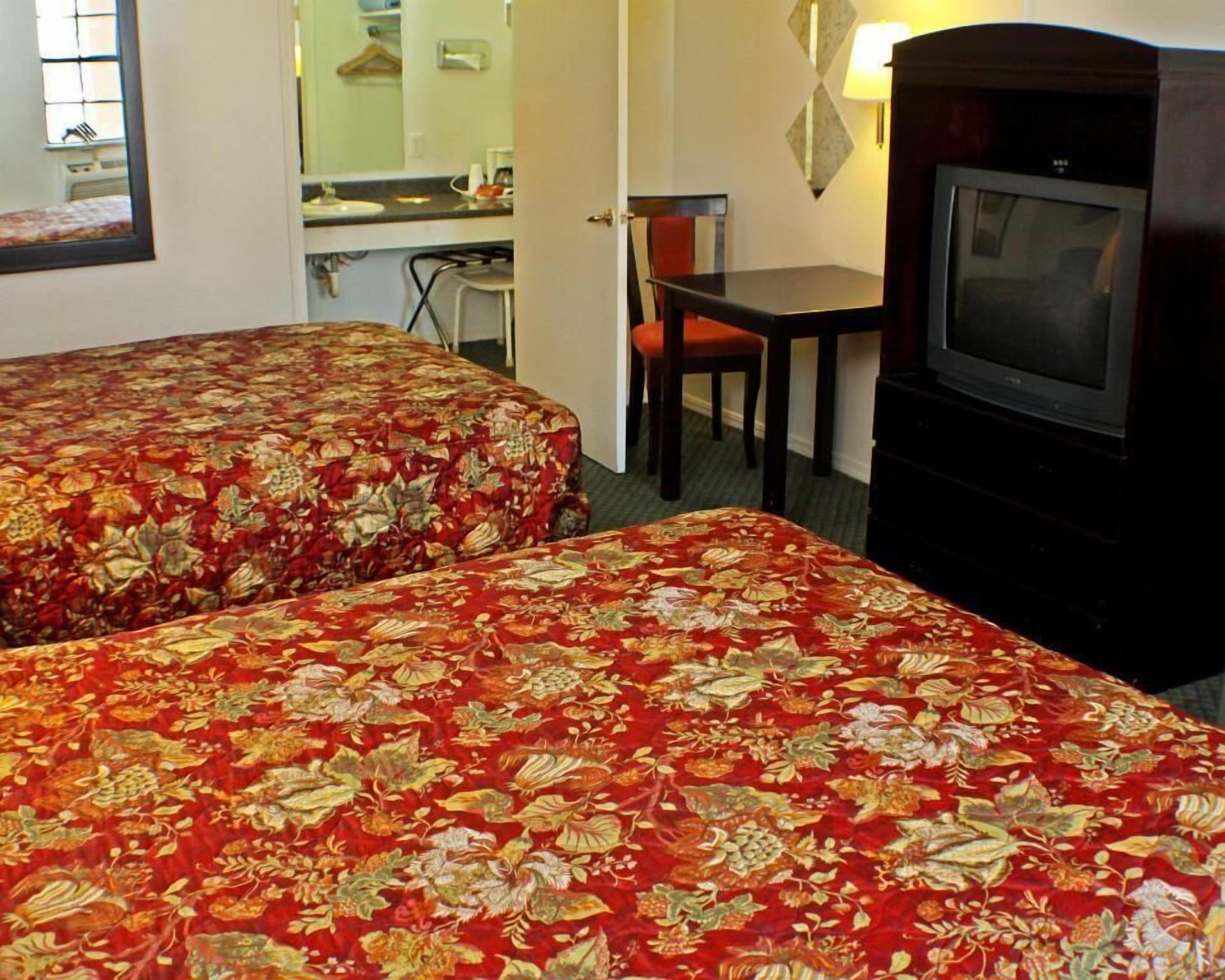 A hotel room with two beds, a television, a desk, and a chair.