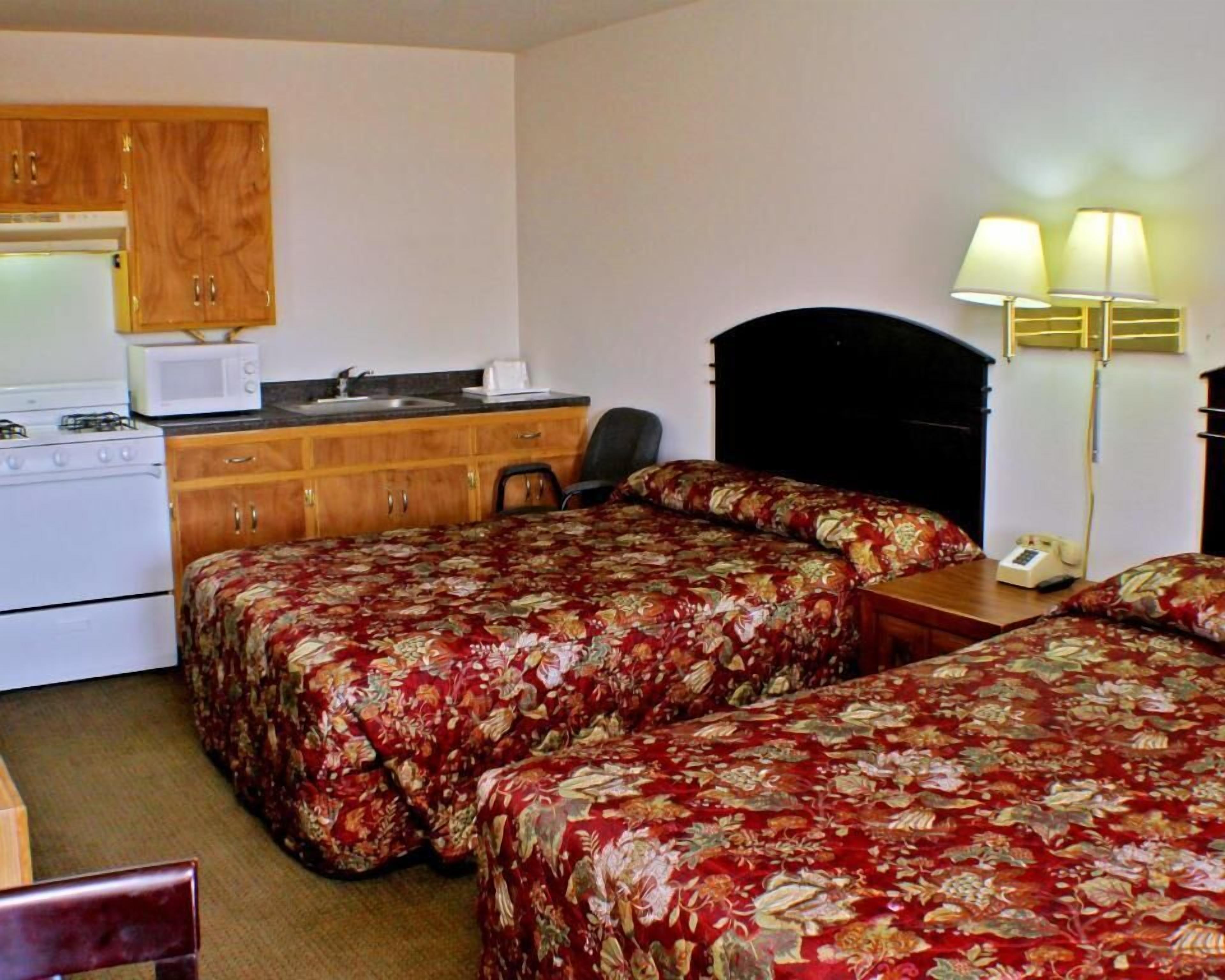 A hotel room with two beds, a kitchenette, a desk, and a telephone.