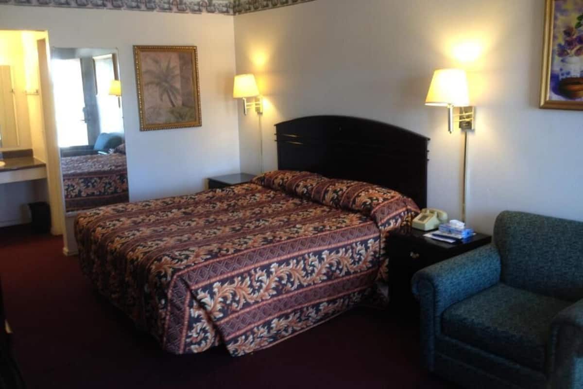 A hotel room with a large bed, two bedside lamps, a chair, and a desk.