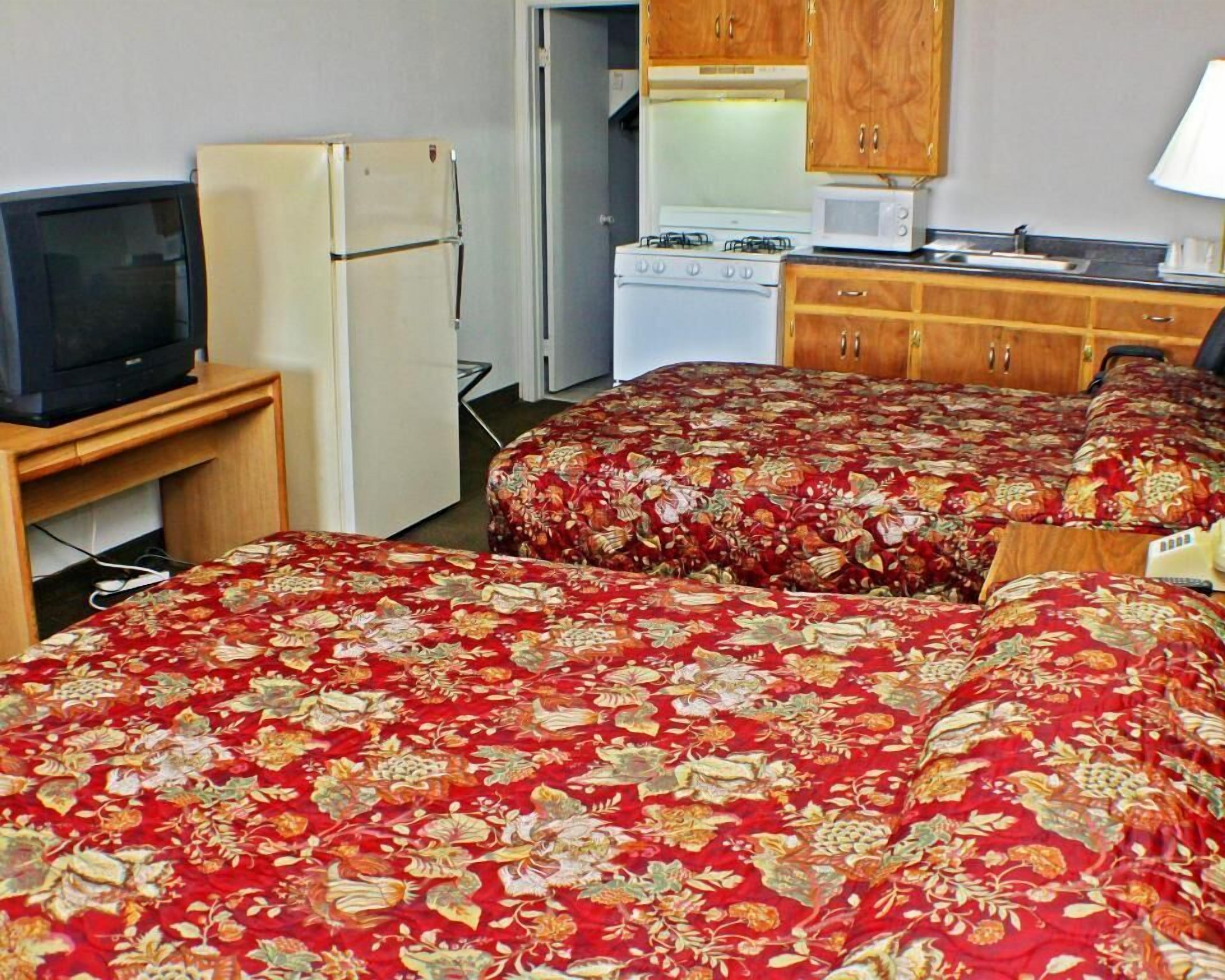 Quarto de hotel com duas camas, televisão, frigorífico, micro-ondas e uma pequena cozinha.