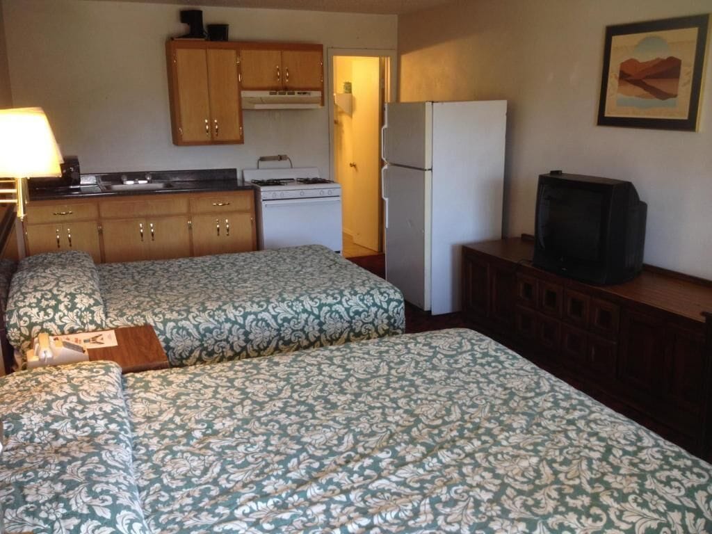 A room with two beds, a television, a refrigerator, a stove, and wooden cabinets.